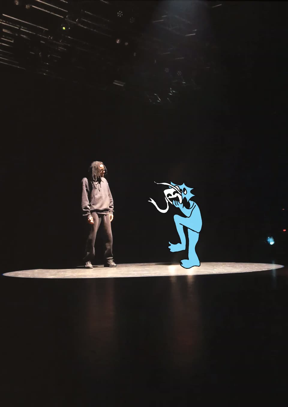 Visuel de l'affiche 2026 : sur un plateau sombre, une artiste de scène face à une grande créature bleue qui tient un masque