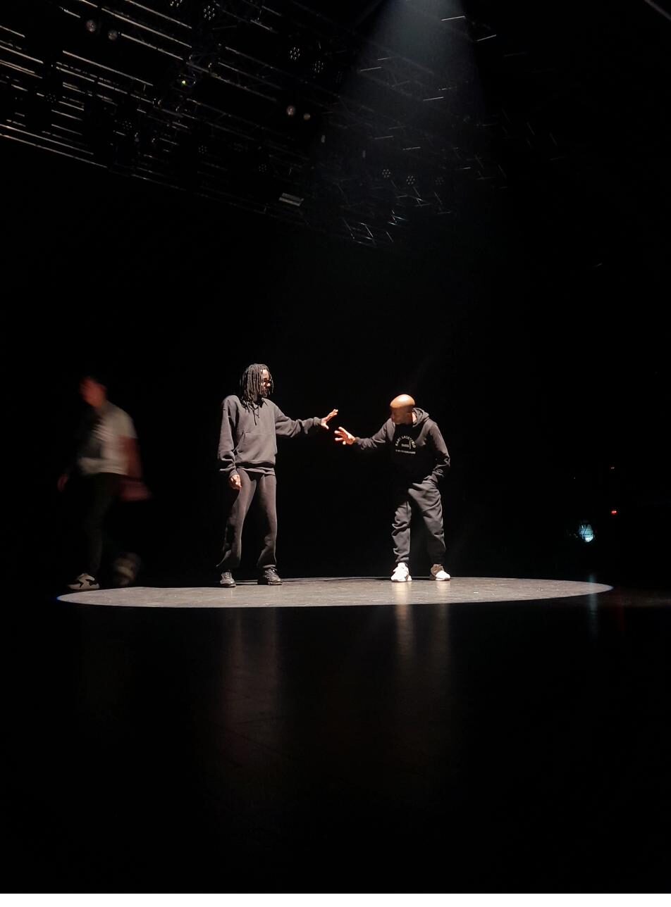 Deux interprètes sur un plateau de théâtre dans la pénombre